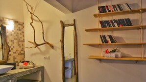 A bathroom with a wooden branch decor, a mirror, and a shelf with books.