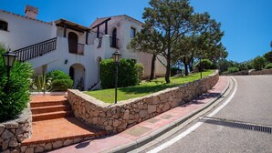 Un edificio blanco con una escalera de piedra que conduce a un balcón, rodeado de vegetación y un muro de piedra.
