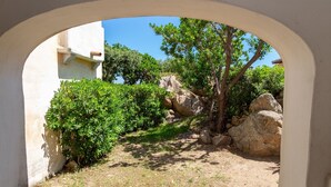 Un patio exterior con un sendero de piedra, arbustos verdes y una gran formación rocosa.
