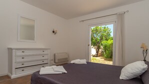 Un dormitorio con cama, cómoda, espejo y vistas al verdor exterior.