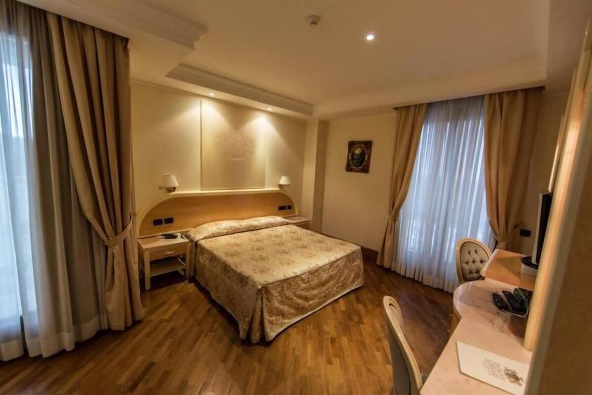 A hotel room with a bed, bedside table, lamp, and a desk with a chair.