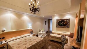 Habitación de hotel con cama doble, sofá, mesita, televisor y candelabro.