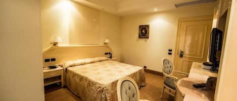 Habitación de hotel con cama, escritorio, silla, televisor y puerta.