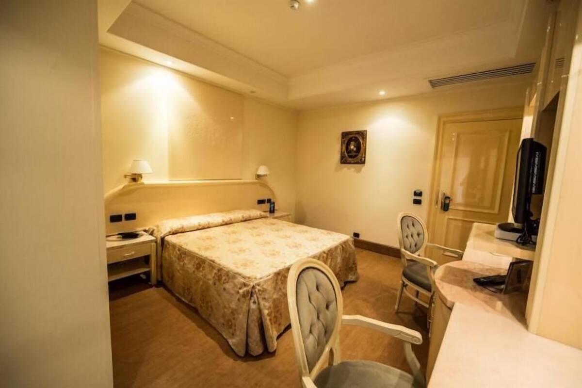 A hotel room with a bed, a desk, a chair, a television, and a door.