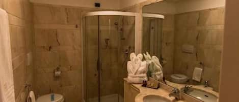 Un baño con cabina de ducha de vidrio, inodoro, bidé, lavamanos con espejo y perchero para toallas.