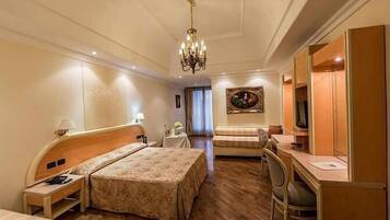 Habitación de hotel con cama, escritorio, silla, televisor y candelabro.