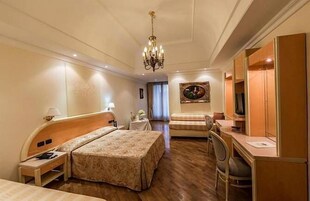 Habitación de hotel con cama, escritorio, silla, televisor y candelabro.