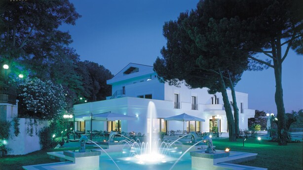 Un hotel moderno con una fuente central, mesas al aire libre y un jardín bien cuidado.