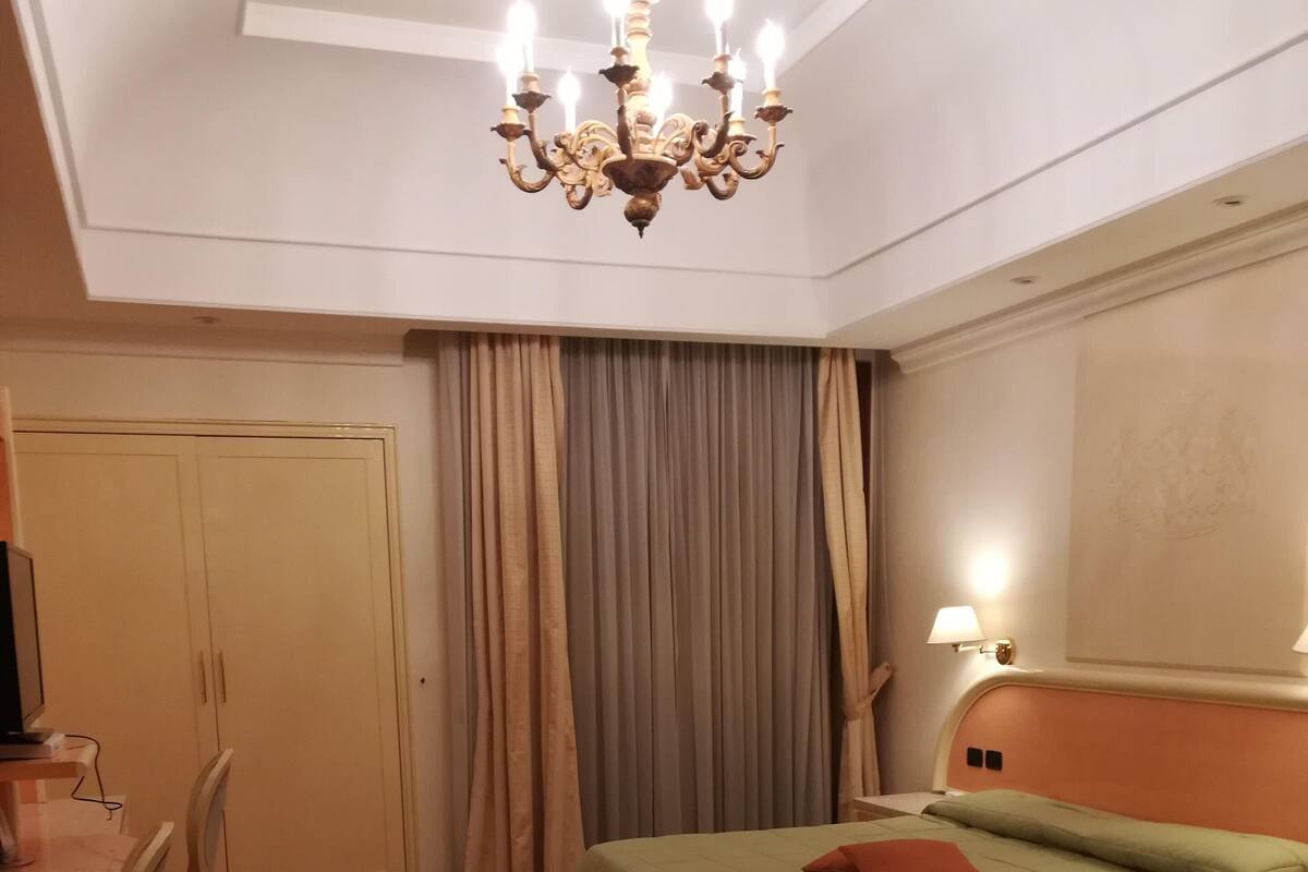 A bedroom with two beds, a desk, a chair, a wardrobe, and a chandelier.