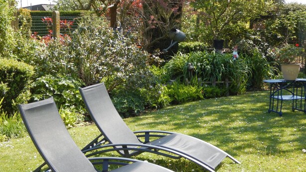 Two lounge chairs in a garden with a hedge and a small table. - B&B La Chrysalide (Mons)