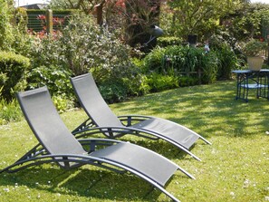 Dos sillones de relax en un jardín con seto y una pequeña mesa.
