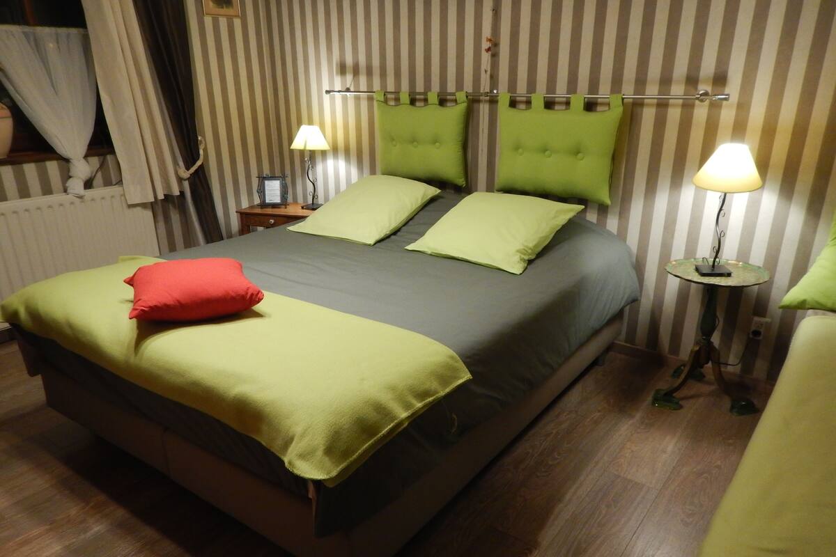 A bed with green bedding and a red pillow, a bedside table with a lamp, and a striped wall.