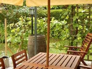 Una mesa y sillas de madera bajo un paraguas amarillo en un jardín con parras de uva.