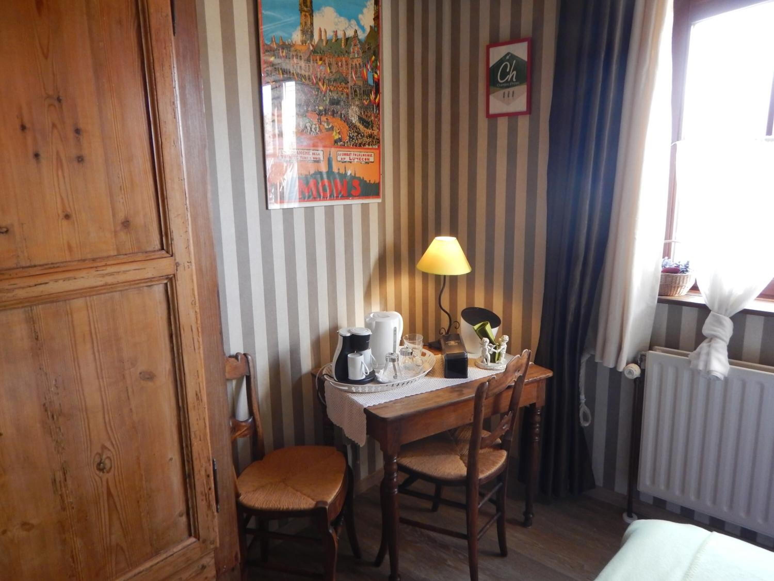 A small dining area with a wooden table, two chairs, a lamp, and a poster on the wall.
