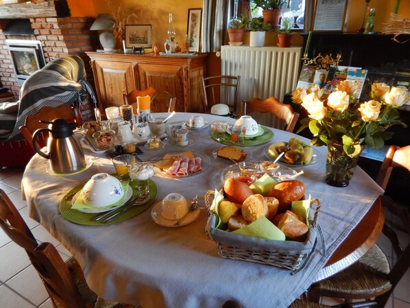 Una mesa de desayuno con diversos platos, un jarrón de flores y un muro de ladrillo al fondo.