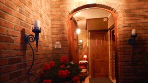 A narrow brick corridor with a wooden door at the end, a small table with a chair, and a potted plant with red flowers. - B&B La Chrysalide (Mons)