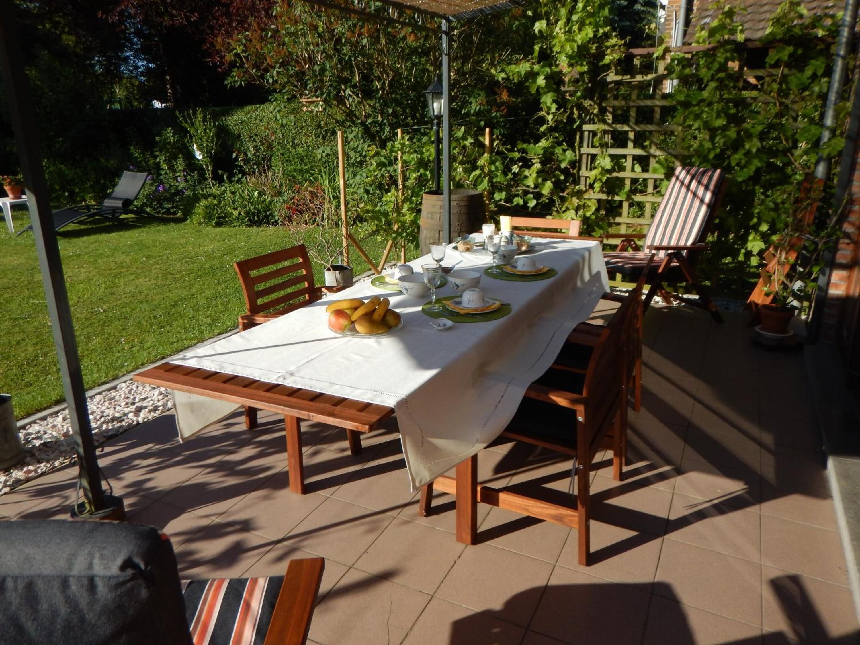 Ein Essbereich im Freien mit einem Tisch für vier Personen, umgeben von Stühlen, in einem Garten.