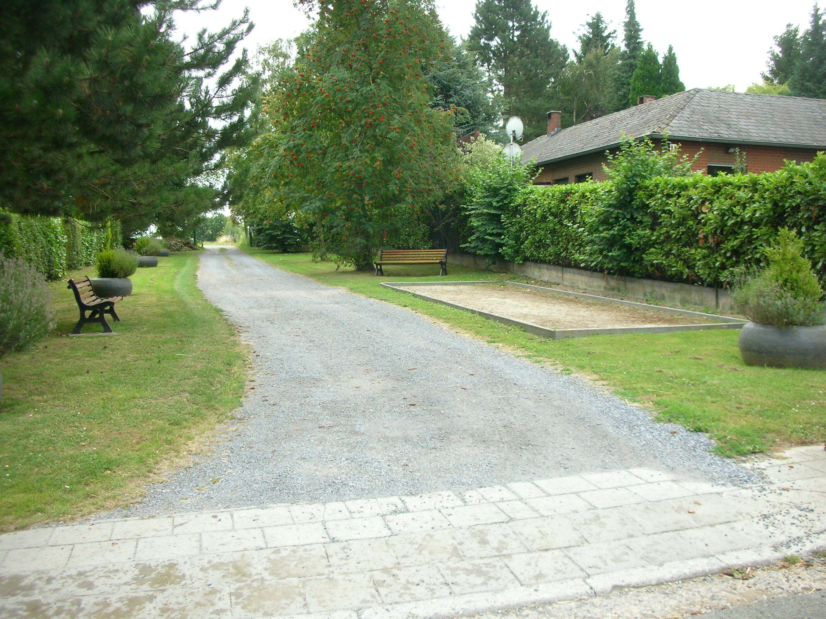 A gravel driveway leading to a house with a bench and a garden area.