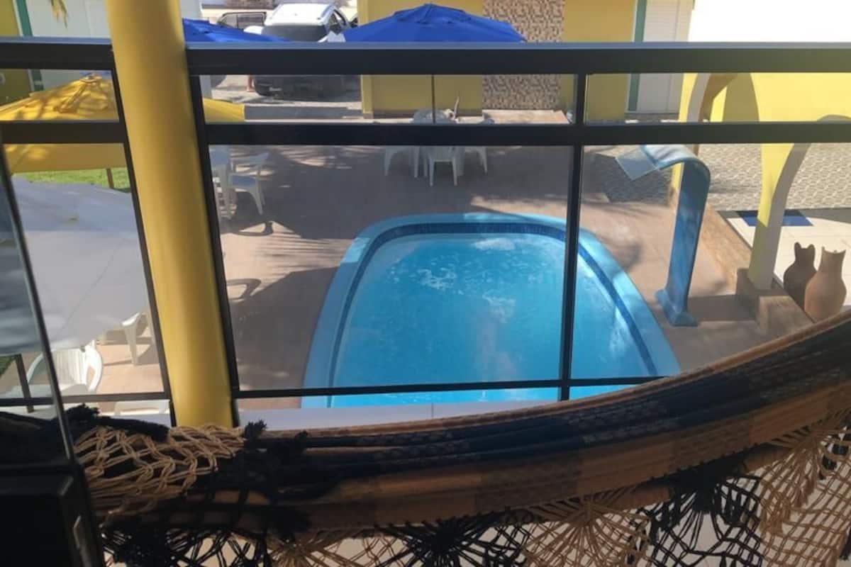 Une vue d’un espace piscine avec un hamac, un mur jaune et un parasol bleu.