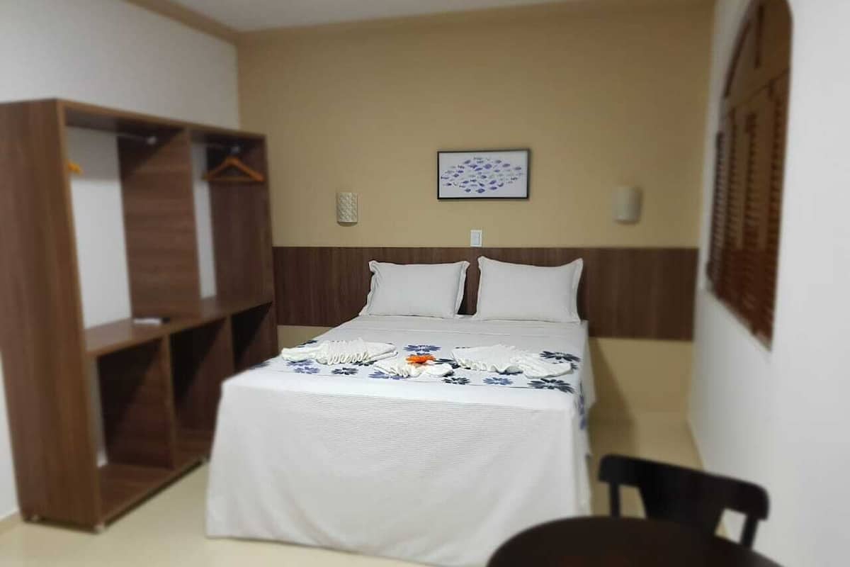 Un lit simple avec une couvre-lit blanche, une armoire en bois et une petite table avec une chaise.