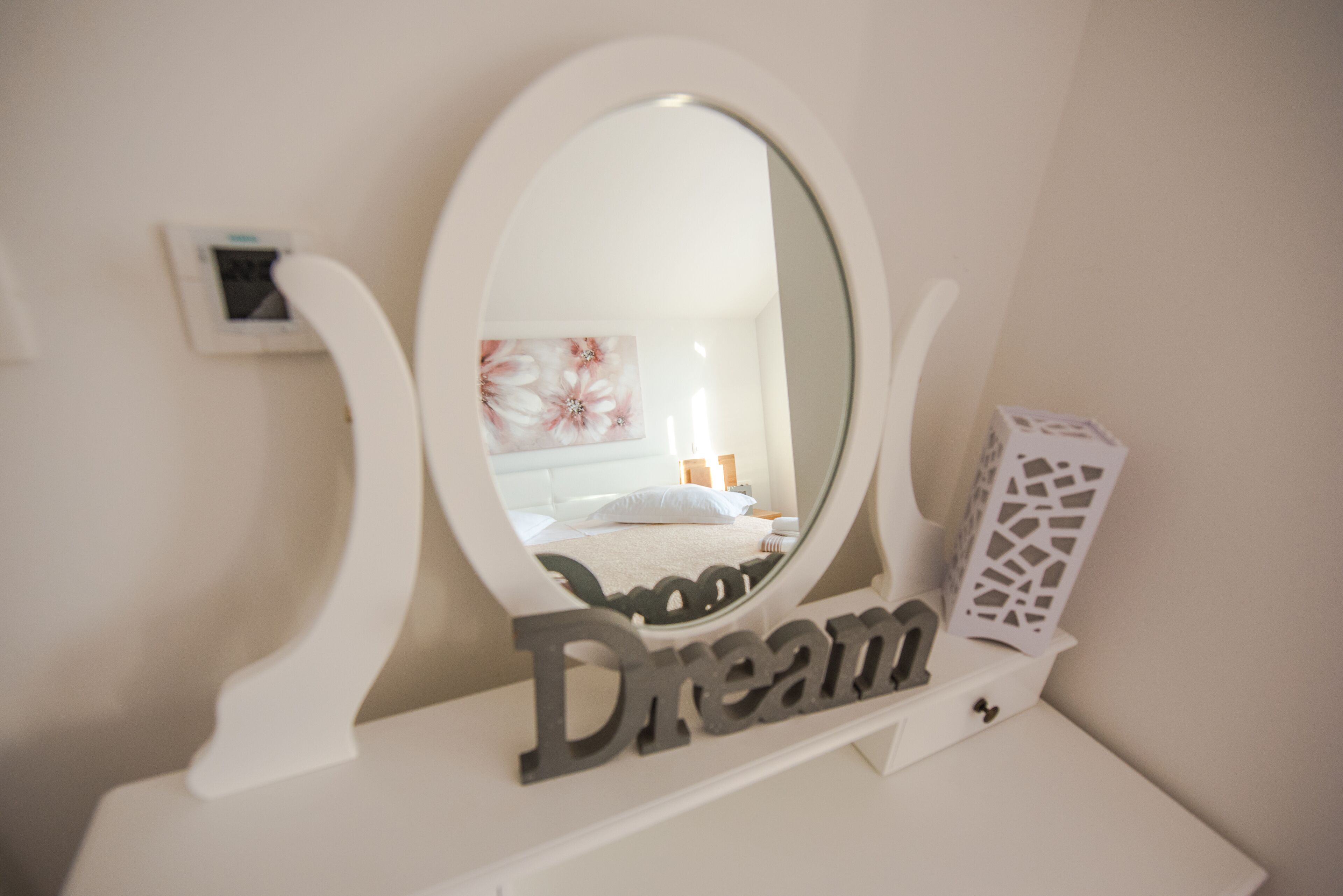 A white vanity with a large oval mirror, a "Dream" sign, and a decorative piece on the wall.