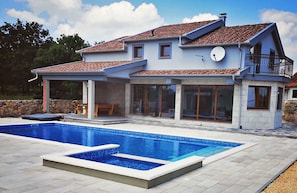 Uma casa de dois andares com piscina, janelas amplas e uma parede de pedra.