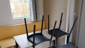 A small, modern room with a single table and four chairs. There is a window with curtains, a bench, and a door with a thermostat on the wall.