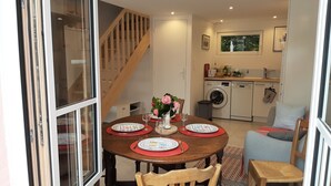 A dining area with a wooden table set for four, a kitchen in the background, and a staircase leading upstairs.