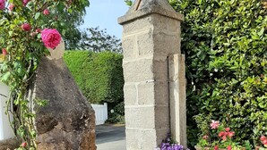 A stone archway with climbing roses and a white picket fence leading to a garden area with various flowers and a stone wall.