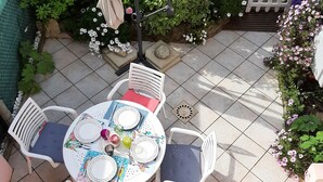 An outdoor patio with a round table set for four, surrounded by white chairs with blue cushions.