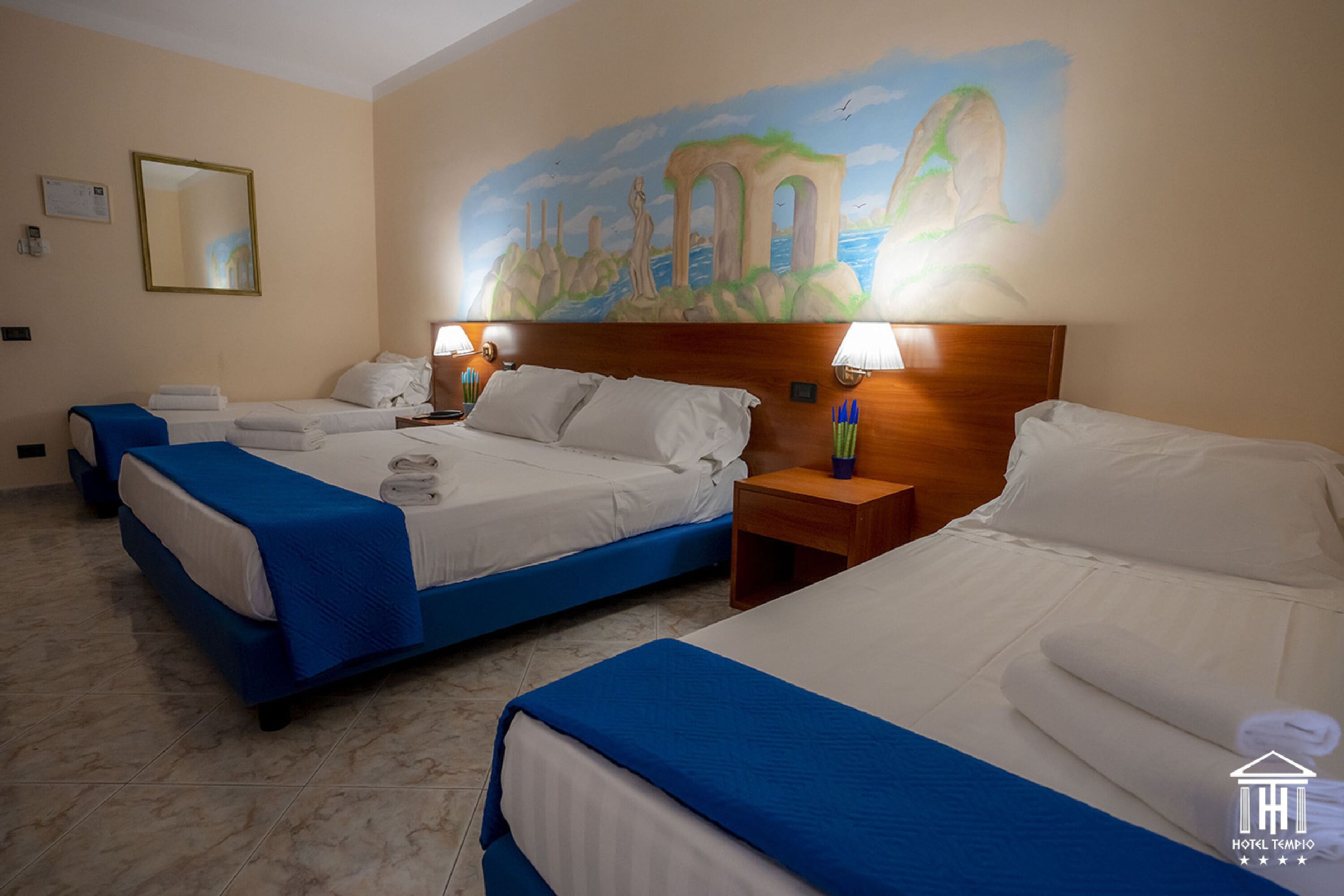 Une chambre d’hôtel avec trois lits, une fresque murale et une tête de lit en bois.