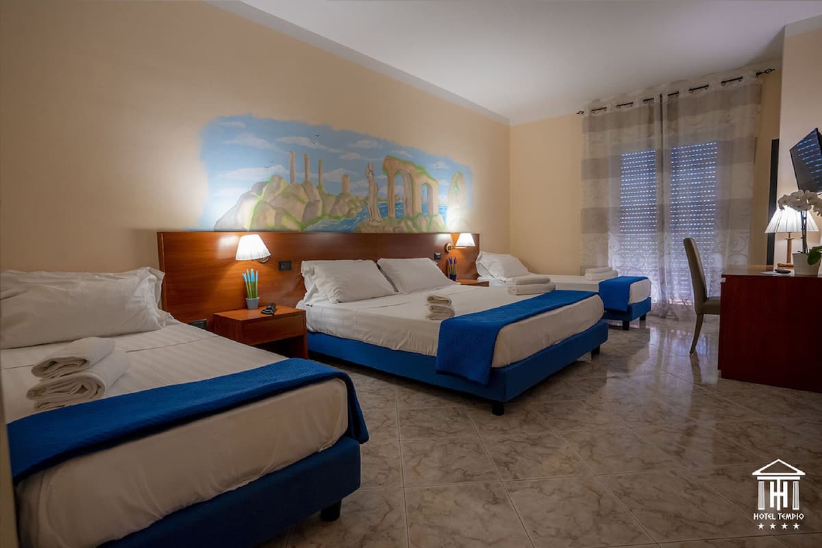 A hotel room with two beds, a desk, and a mural on the wall.
