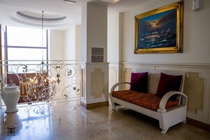 A hotel lobby with a white sofa, a chandelier, a painting, and a sign with directions.