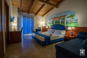 Una habitación de hotel con cama, escritorio, silla, mesita de noche y un cuadro en la pared.