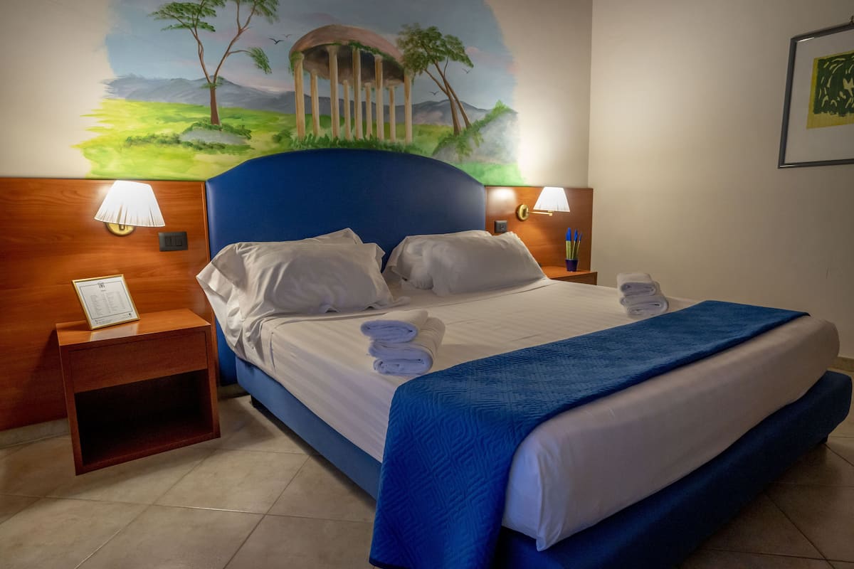 A hotel room with a large bed, two bedside lamps, a nightstand, and a mural on the wall.