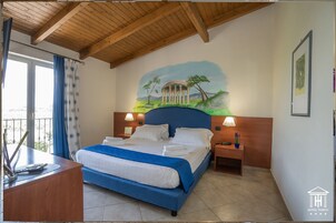 Habitación de hotel con una cama, dos mesitas de noche, un escritorio con una silla, una ventana con cortinas y un mural en la pared.