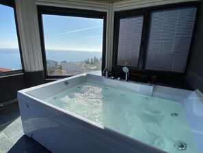 A large, rectangular hot tub with a view of the city through large windows.