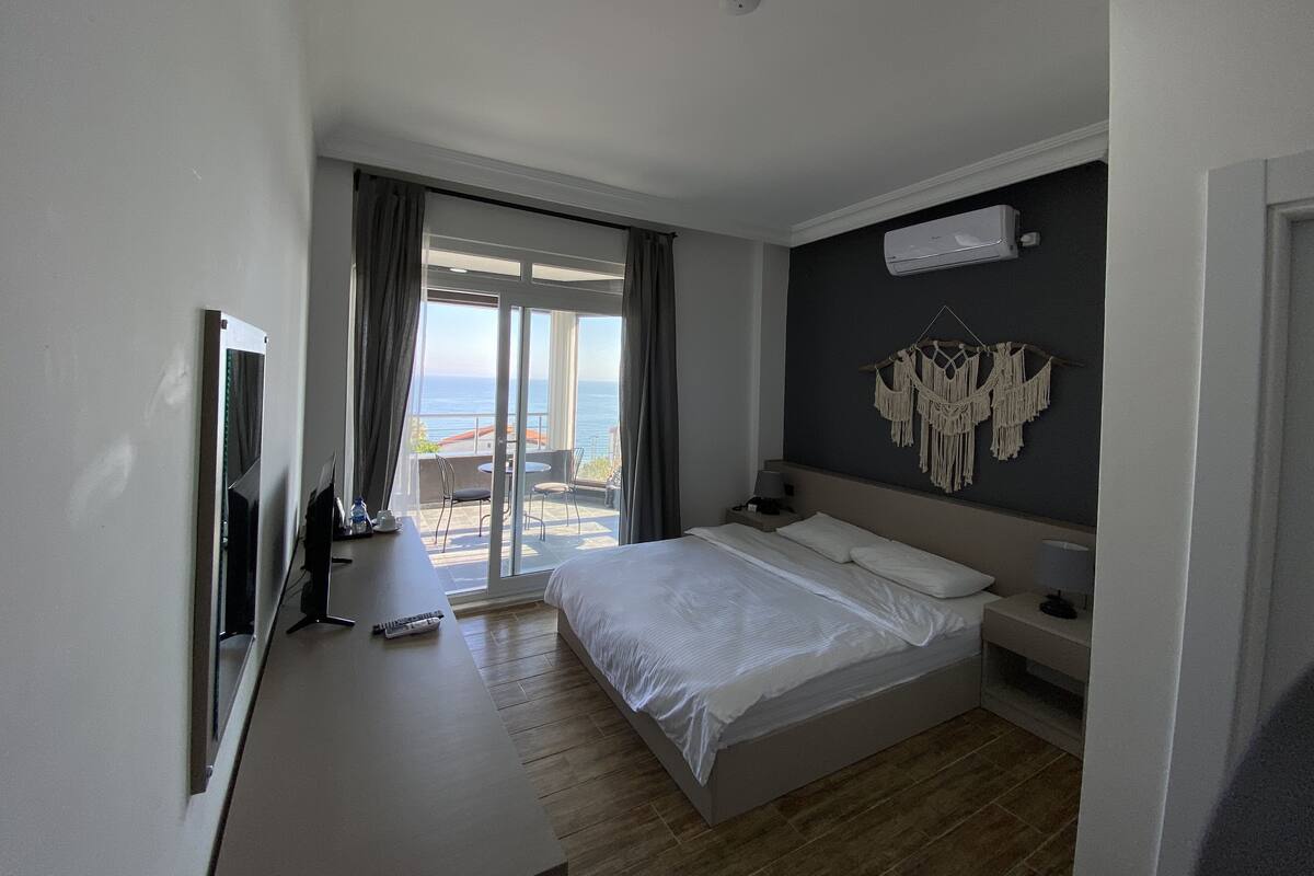 Habitación de hotel con cama, televisión, balcón y vista al mar, además de un tapiz de macramé en la pared.