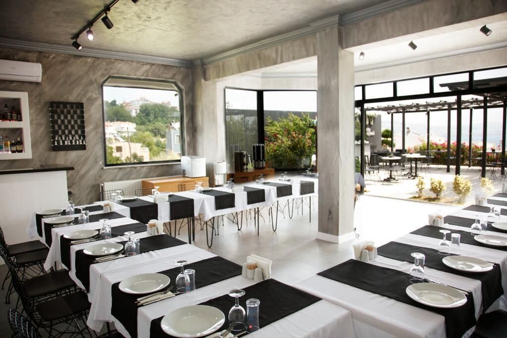 Un comedor moderno con mesas dispuestas para el servicio, una cocina al fondo y vistas al exterior.