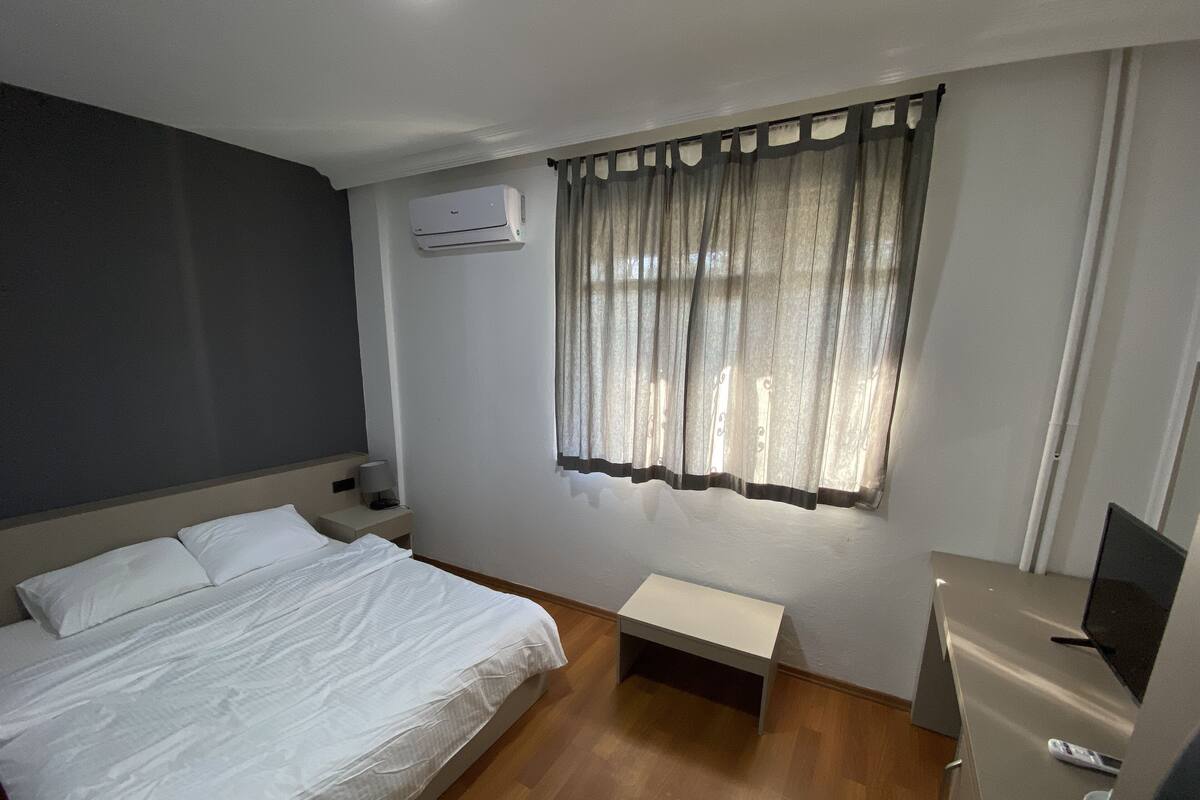 Habitación de hotel con cama, mesita de noche, televisión y aire acondicionado.
