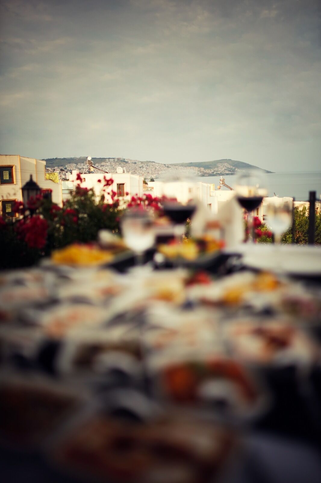 Vista borrosa de un comedor con una mesa dispuesta para una comida, con vistas a un paisaje urbano que incluye edificios y una montaña distante.