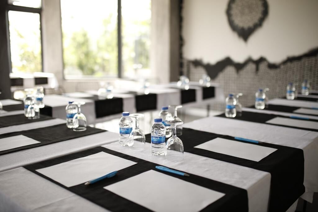 Una sala conferenze con tavoli preparati per una riunione, dotata di bottiglie d'acqua e penne.