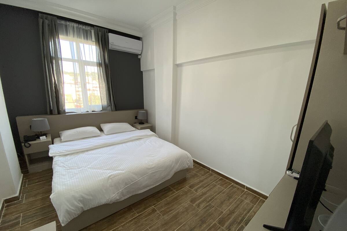 Una habitación de hotel con una cama, una mesita de noche, una lámpara, un equipo de aire acondicionado y un televisor.