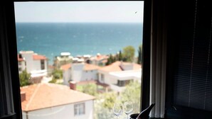 A bathtub with rose petals, two wine glasses, and a view of the sea and buildings. - No57 Suites (Sinop)