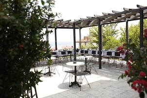 An outdoor patio area with round tables and chairs, a pergola structure, and a view of the sea.