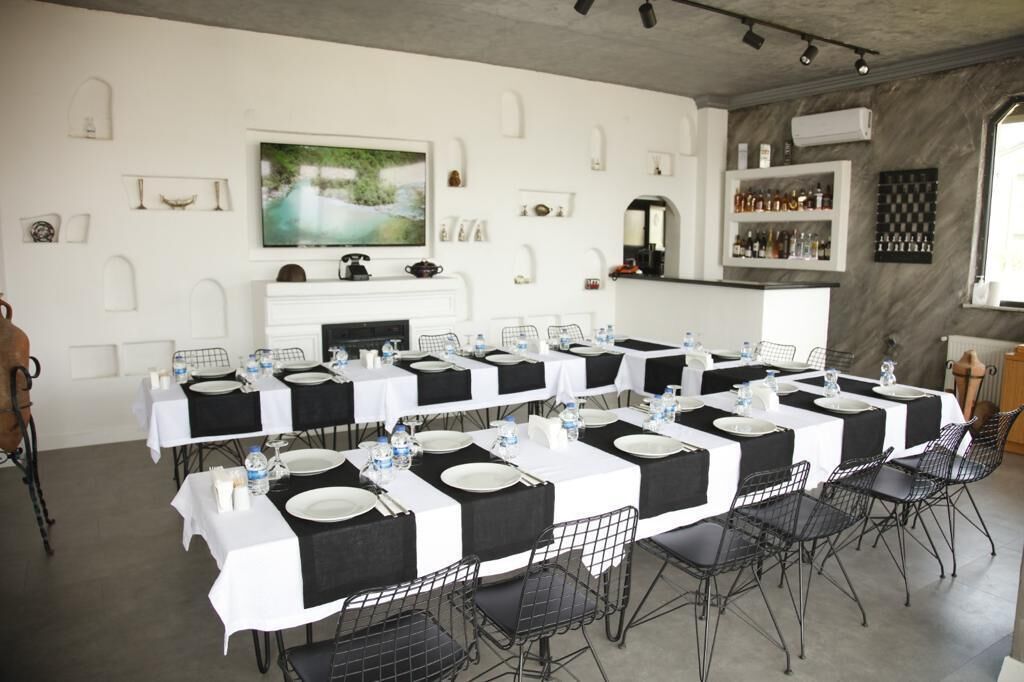 A dining area with long tables set for multiple guests, a fireplace, and a kitchen area with shelves of bottles.