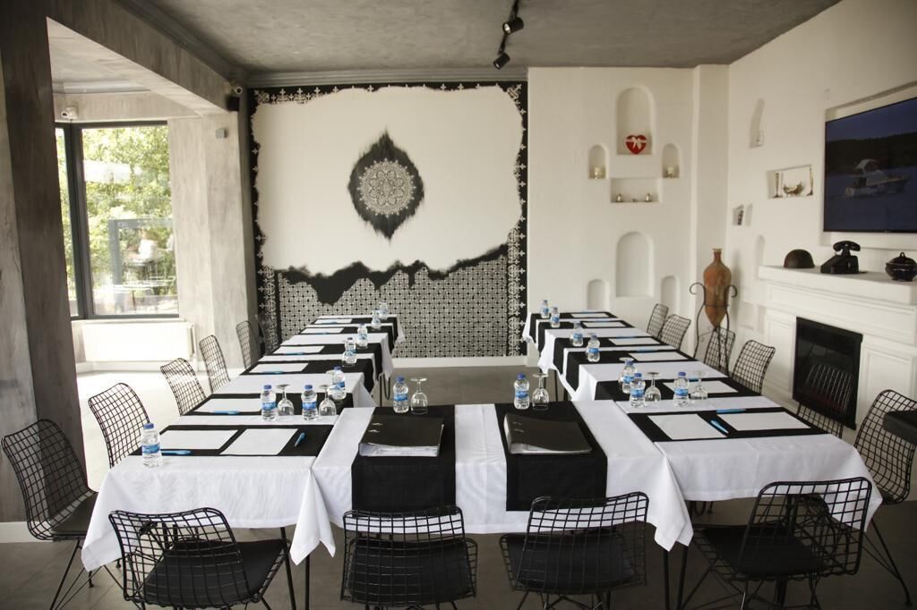 A conference room with long tables, black wire chairs, and white tablecloths.