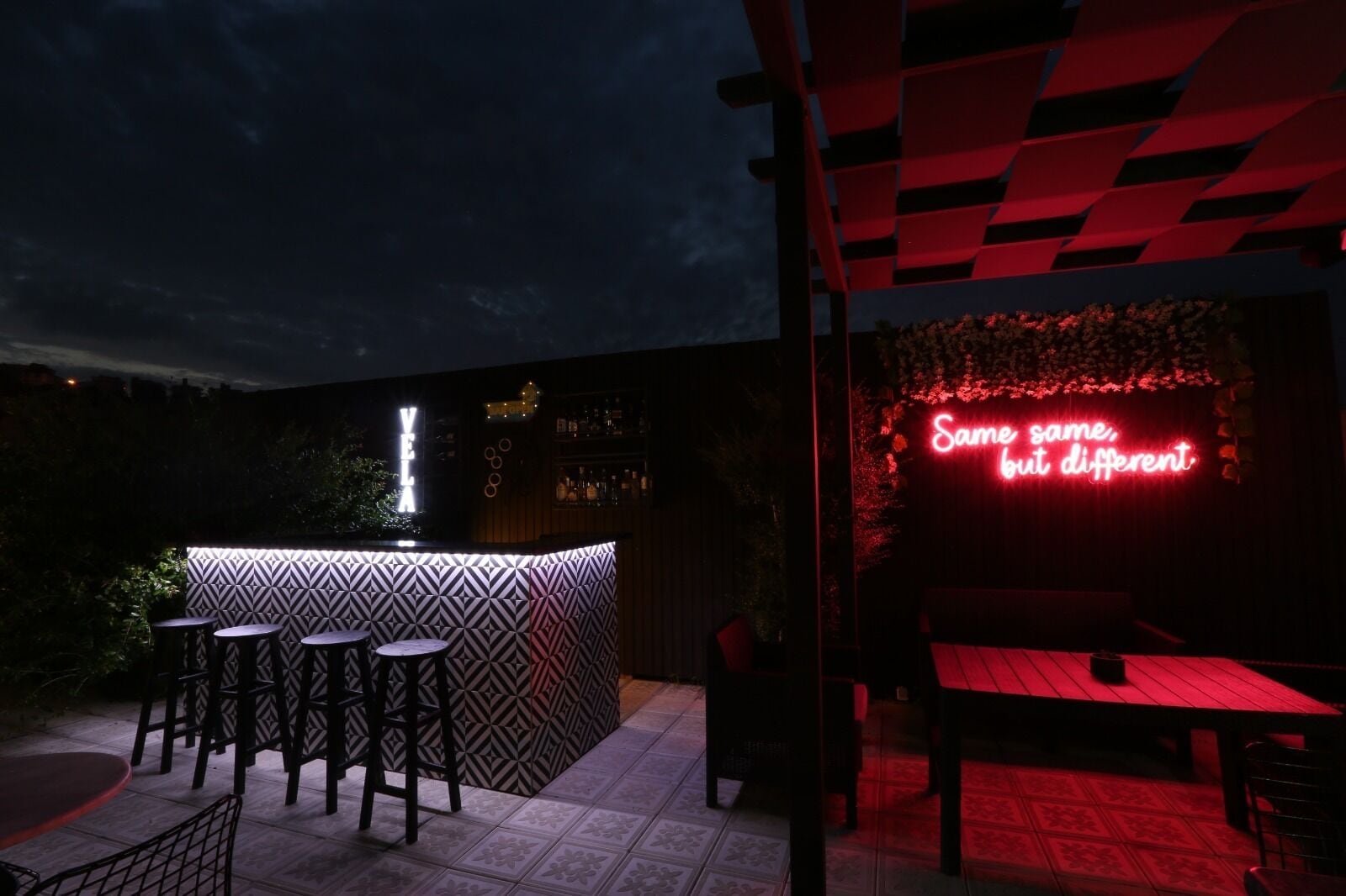 An outdoor bar area with a neon sign reading "Same same, but different."