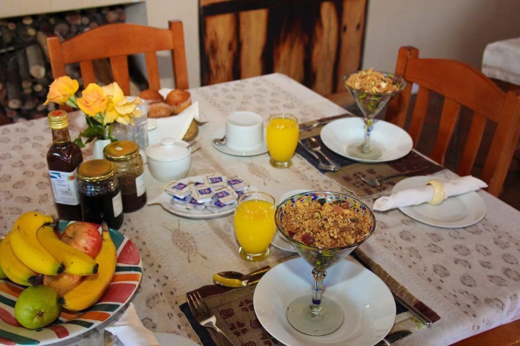 A breakfast table set with plates, bowls, and a variety of food items including fruits and a glass of orange juice.