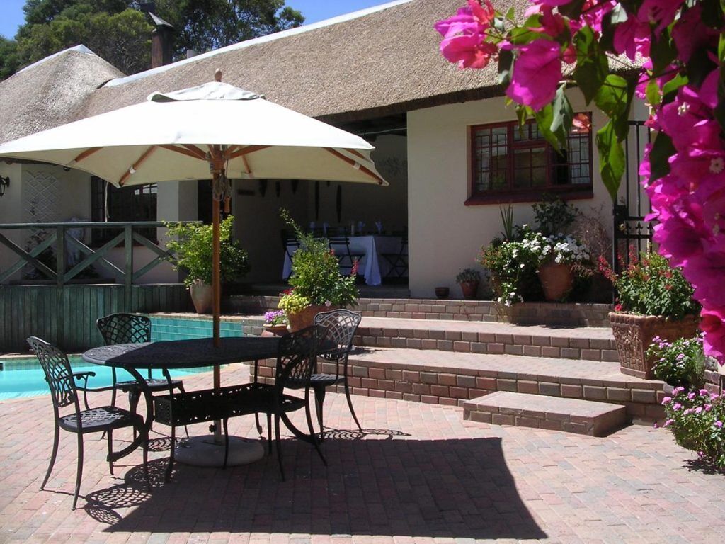 Un patio exterior con mesa y sillas, una piscina y plantas en macetas.